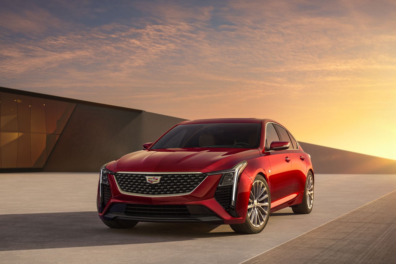 A red Cadillac CT4 with a dark grille and silver wheels, parked on a paved surface at sunset.
