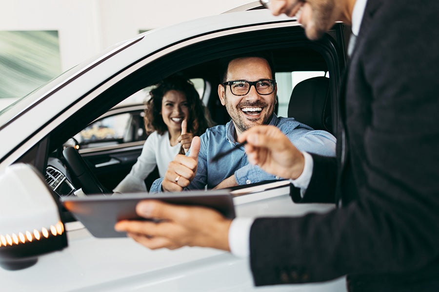 two happy people in a car with a sales person outside of the vehicle talking to them